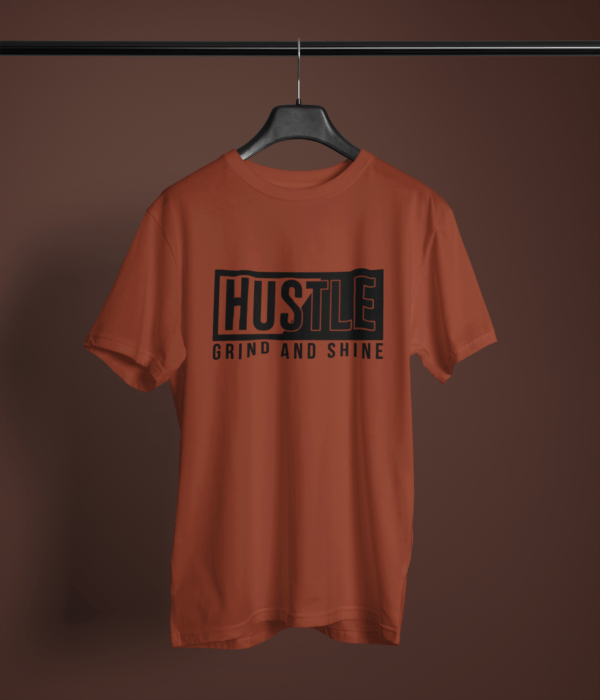 brick red color hustle grind and shine graphic printed t-shirt on a hanger